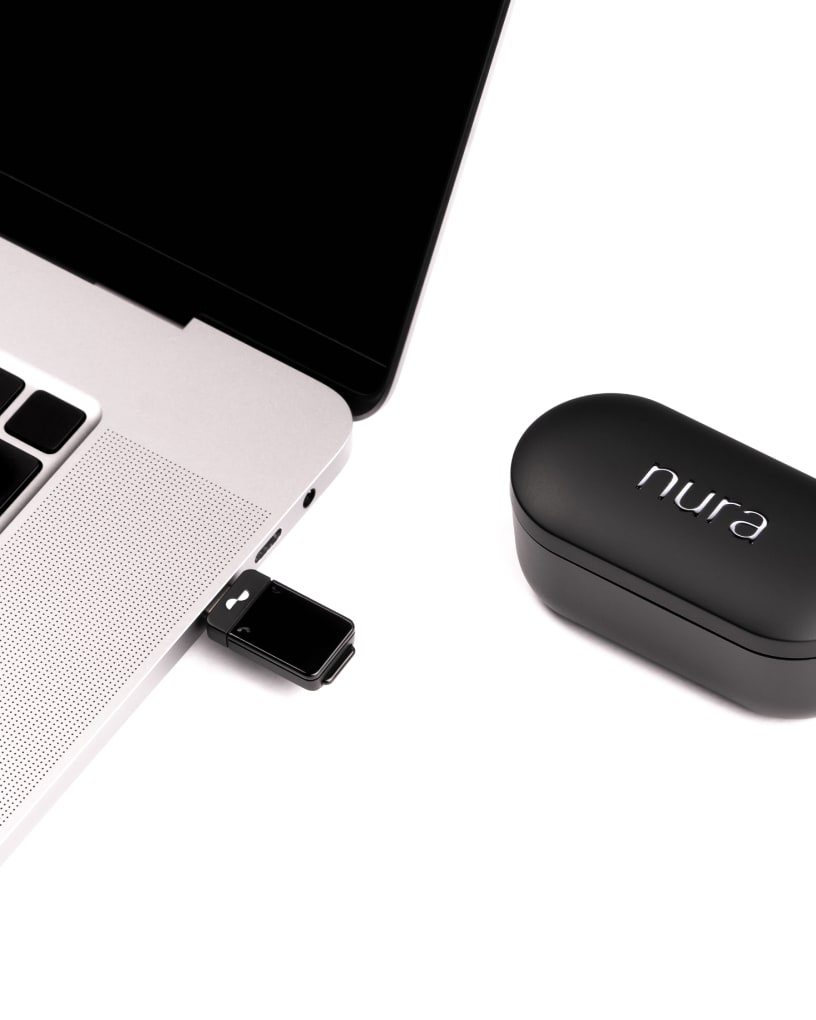 Transmitter plugged into MacBook Pro next to NuraTrue Pro charging case